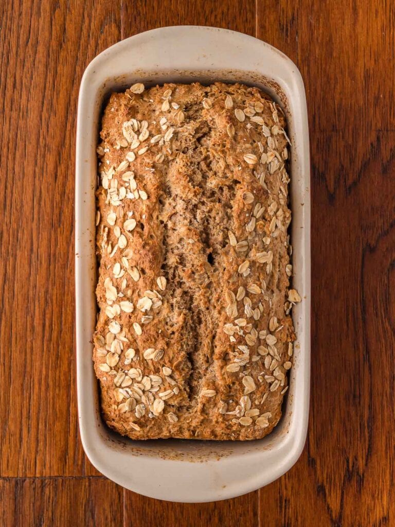 Cooked brown bread on in a bread pan on a wooden table.