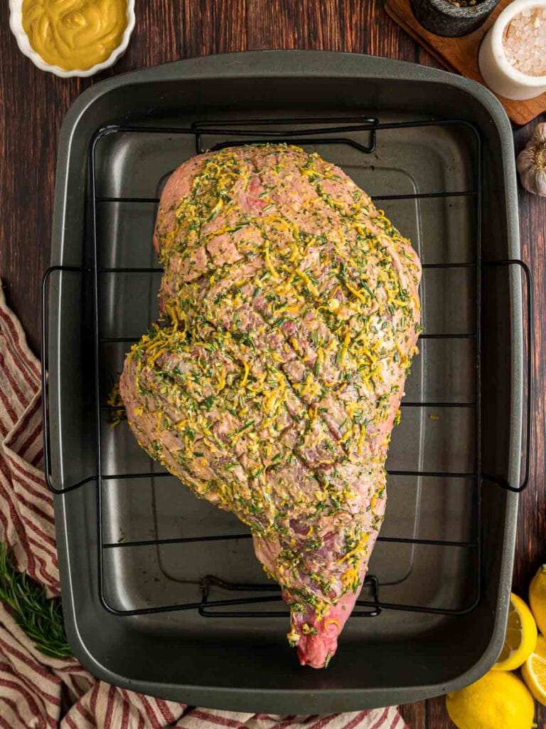 a large leg of lamb with a herb rub in a roasting pan.