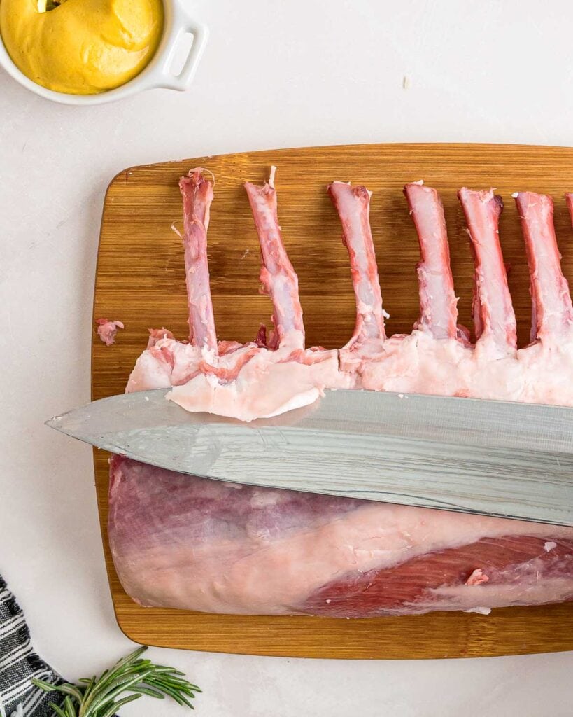 A knife trimming the fat off a rack of lamb.