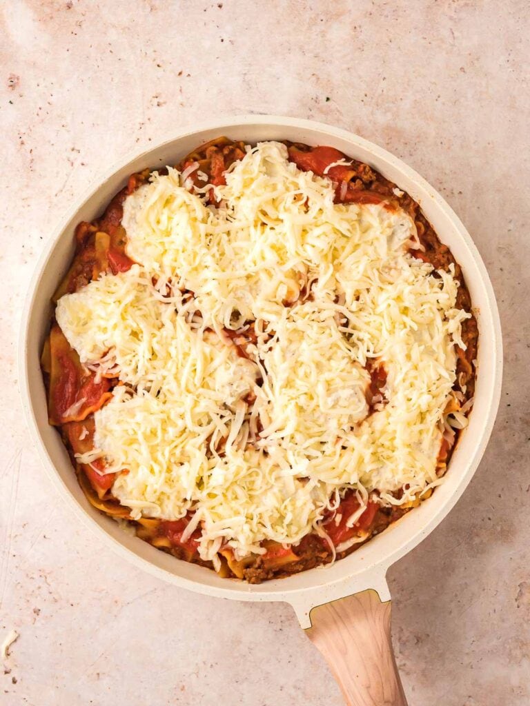 Uncooked Skillet Lasagna with ricotta and cheese on top in a pan.