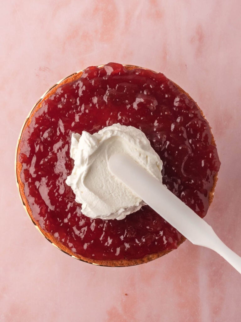 Strawberry Jam and whipped cream being spread onto the victoria sponge.