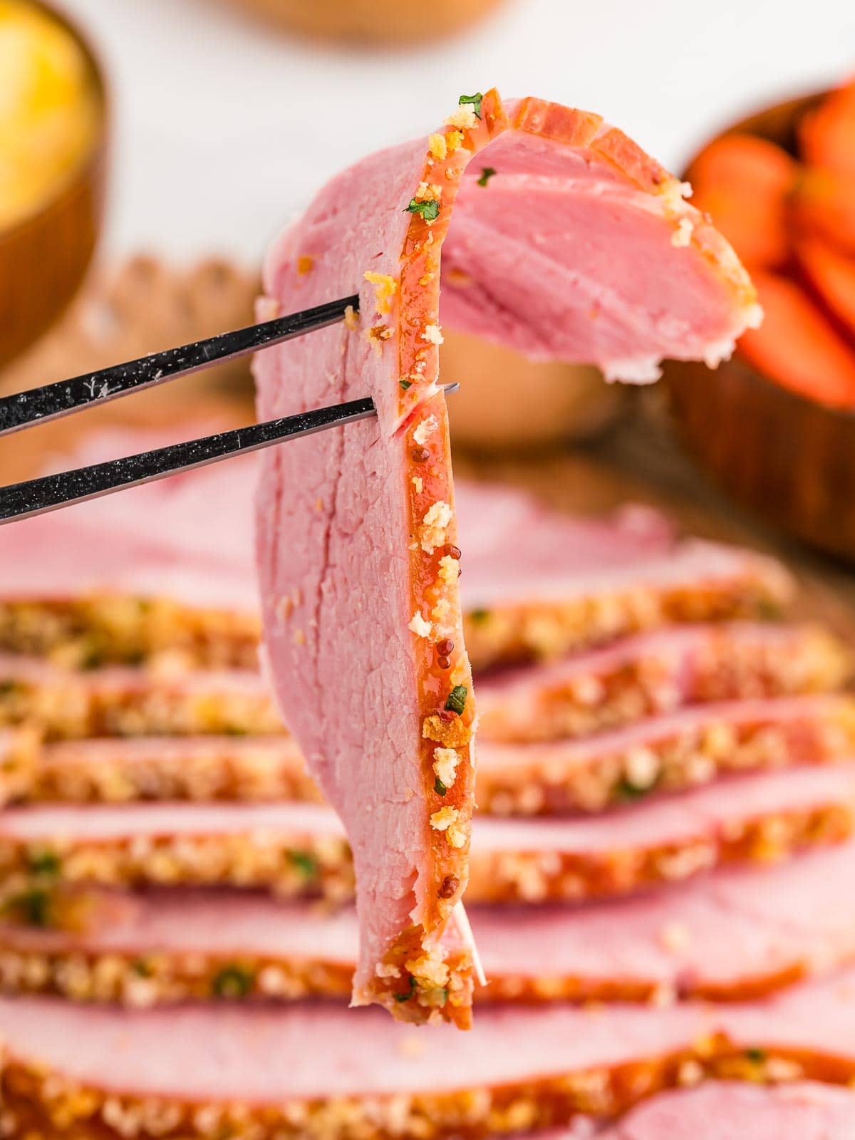 A slice of herb crusted baked ham on a fork.