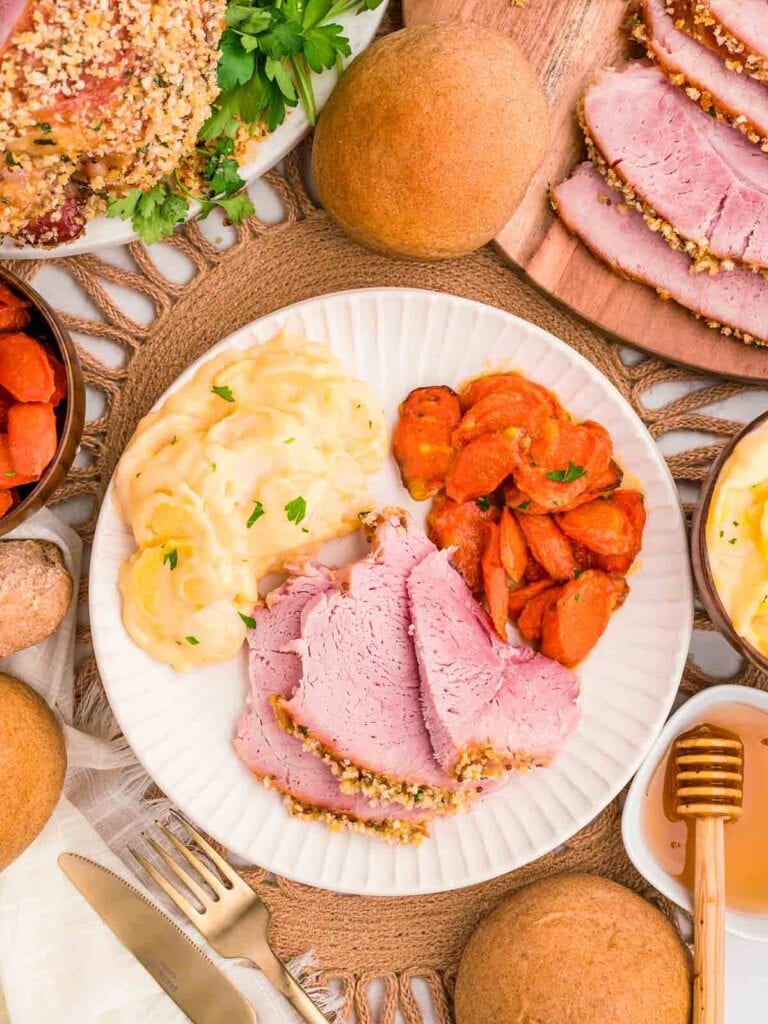 A plate of herb crusted baked ham with carrots and garlic potatoes.