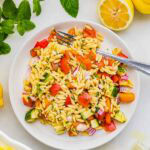 Overhead view of the Orzo Pasta Salad plated with a fork and lemons in the background.