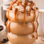 Up close of a Tres Leches Iced Coffee with whipped cream, cinnamon and caramel drizzled on top and running down the side of the glass.