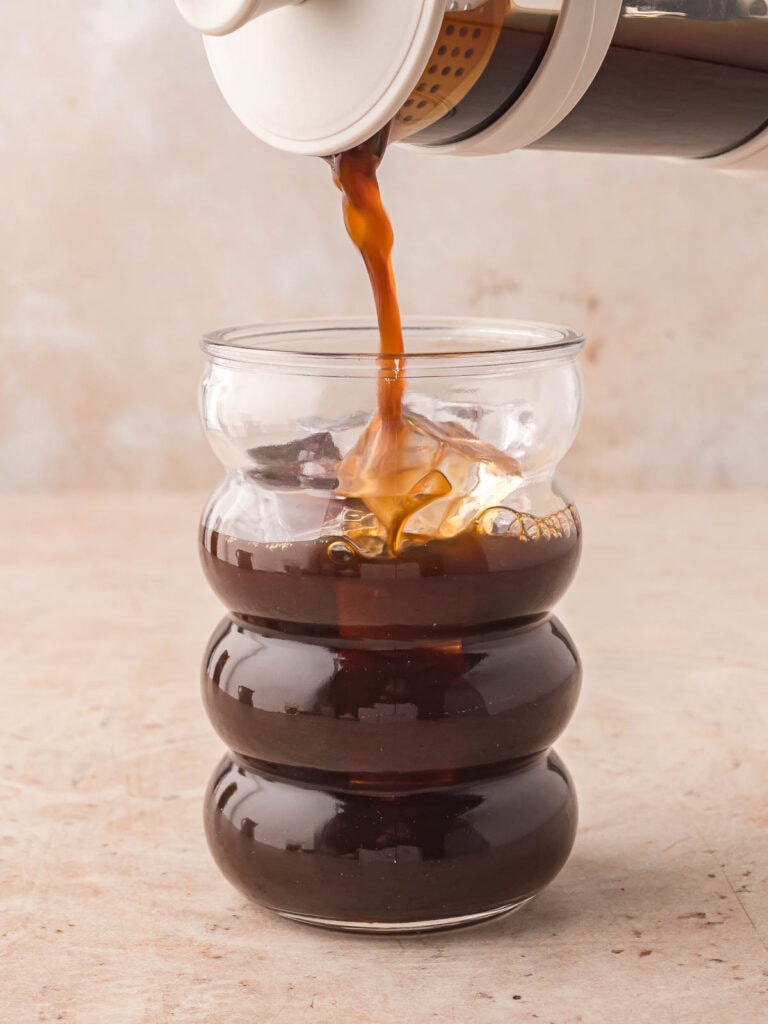 Coffee being poured into a glass with ice.