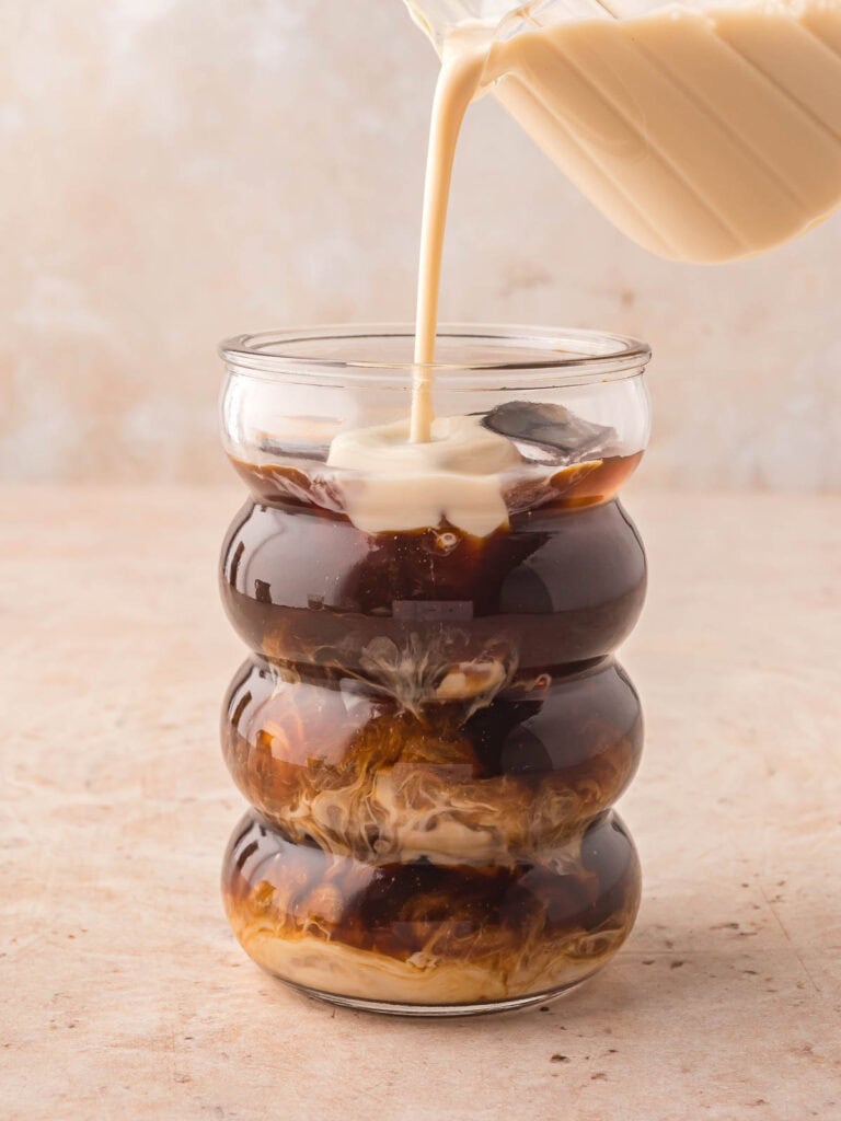 The milk mixture being poured into the glass with the coffee.