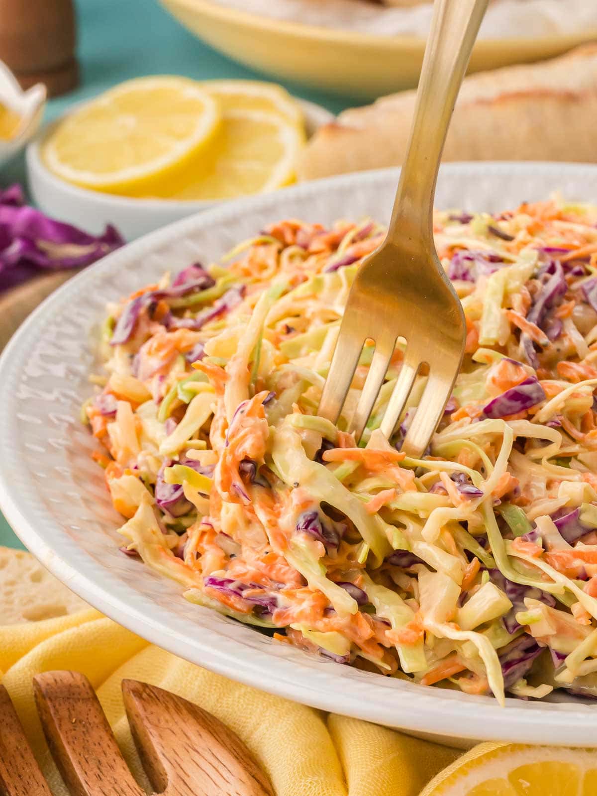 Close-up of creamy coleslaw with a gold fork scooping a bite, showing the colorful cabbage and carrots.