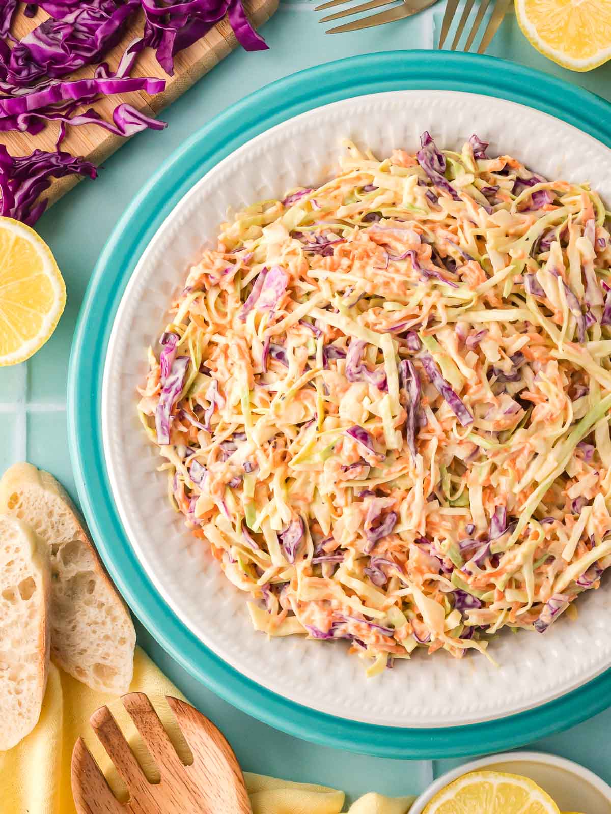 Bowl of creamy homemade coleslaw with green and purple cabbage, surrounded by lemon slices and fresh bread.