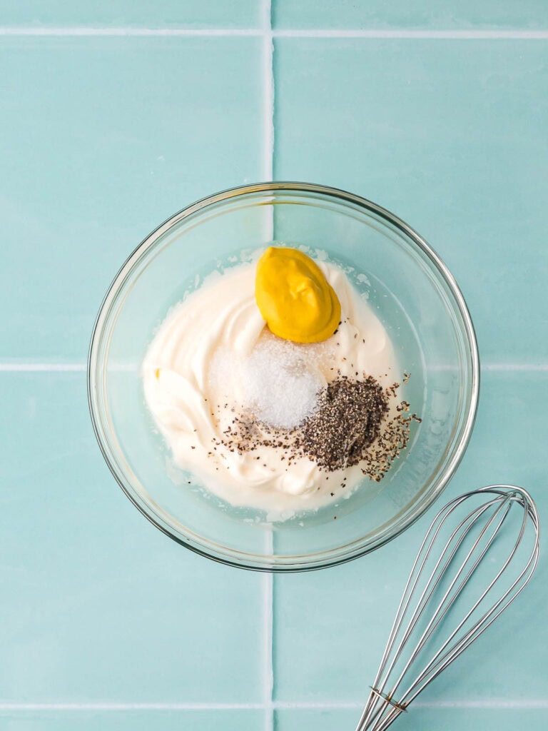 Mayonnaise, mustard, salt, sugar, and pepper added to a small glass bowl before mixing.