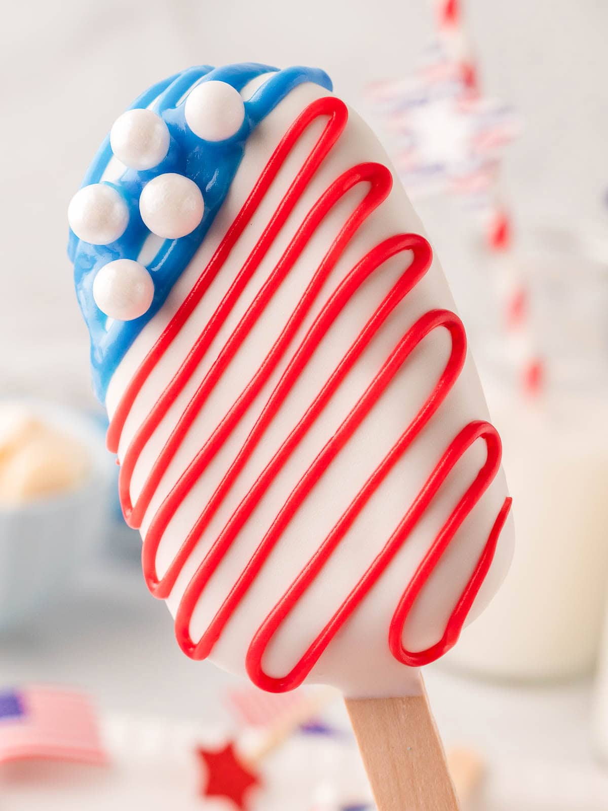 Single cakesicle decorated with red stripes, blue icing, and pearl sprinkles in a star pattern