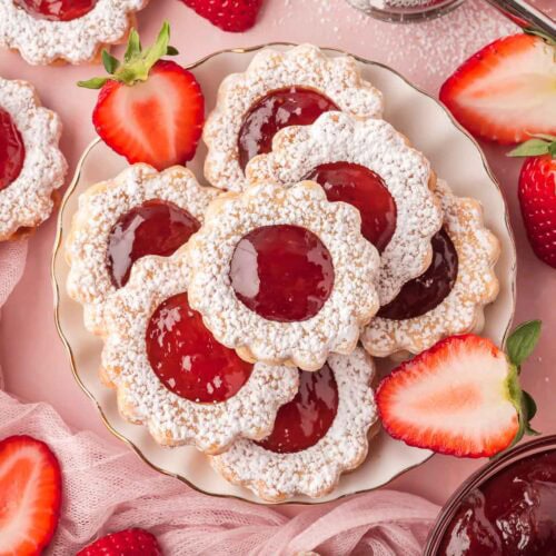 Plate of strawberry pie cookies surrounded by halved strawberries and pink netting for serving.