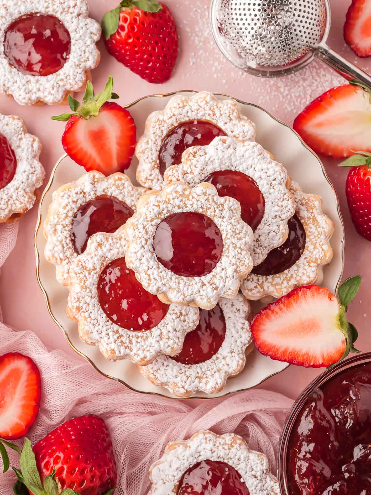 Plate of strawberry pie cookies surrounded by halved strawberries and pink netting for serving.