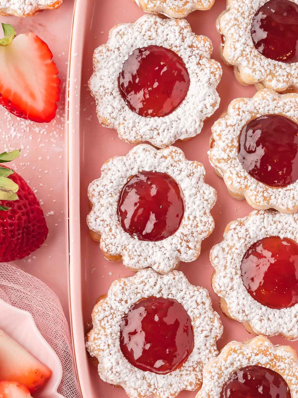 Close-up of finished strawberry pie cookies with jam centers and powdered sugar on a pink plate.
