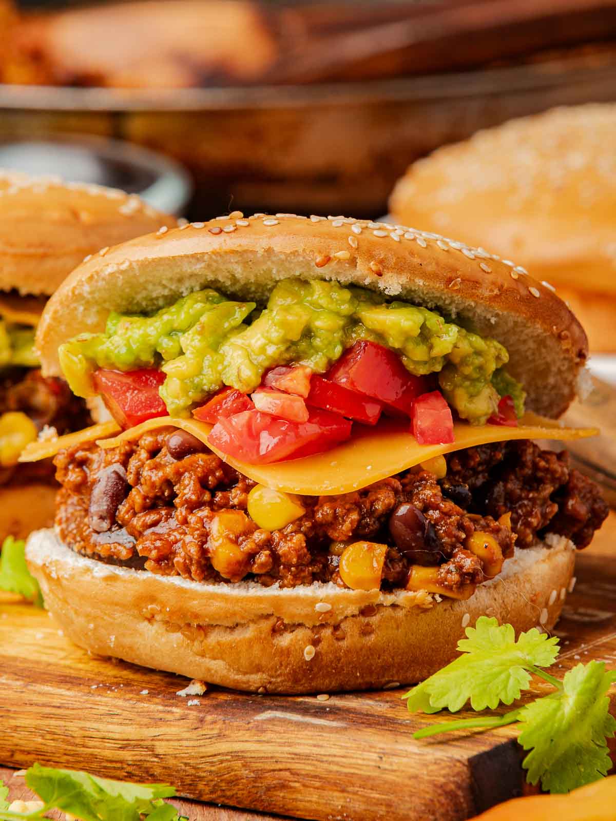 Cheesy Taco Sloppy Joe with all the toppings stacked on a toasted sesame bun and surrounded by fresh cilantro.