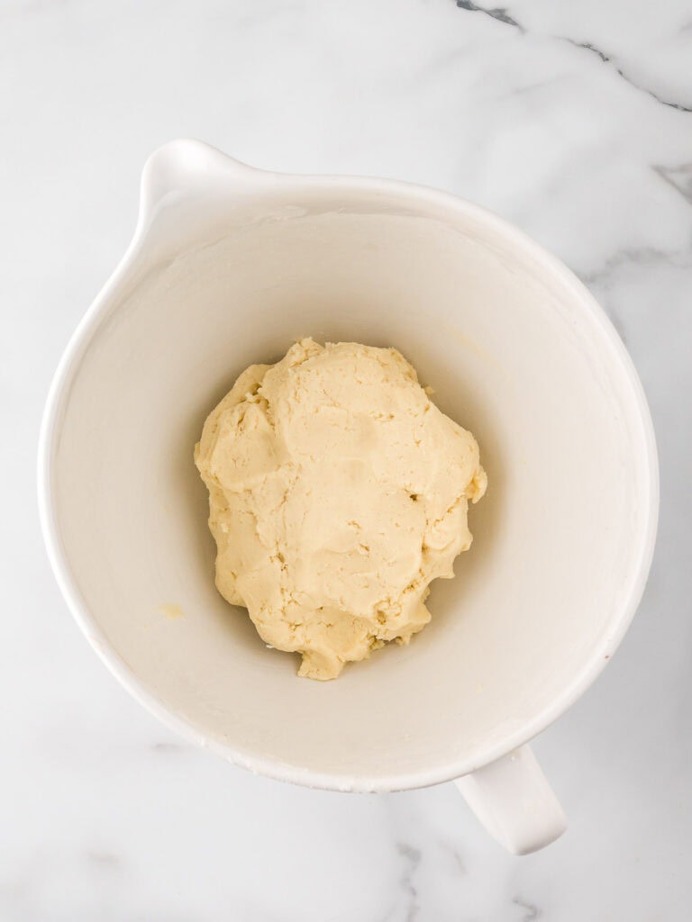 A white mixing bowl filled with smooth vanilla cake and frosting dough, mixed to the perfect consistency.

