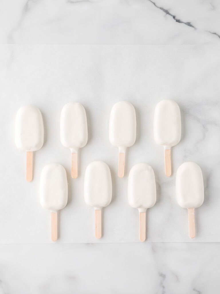 A batch of white chocolate-coated cakesicles lined up on parchment paper, waiting to be decorated.