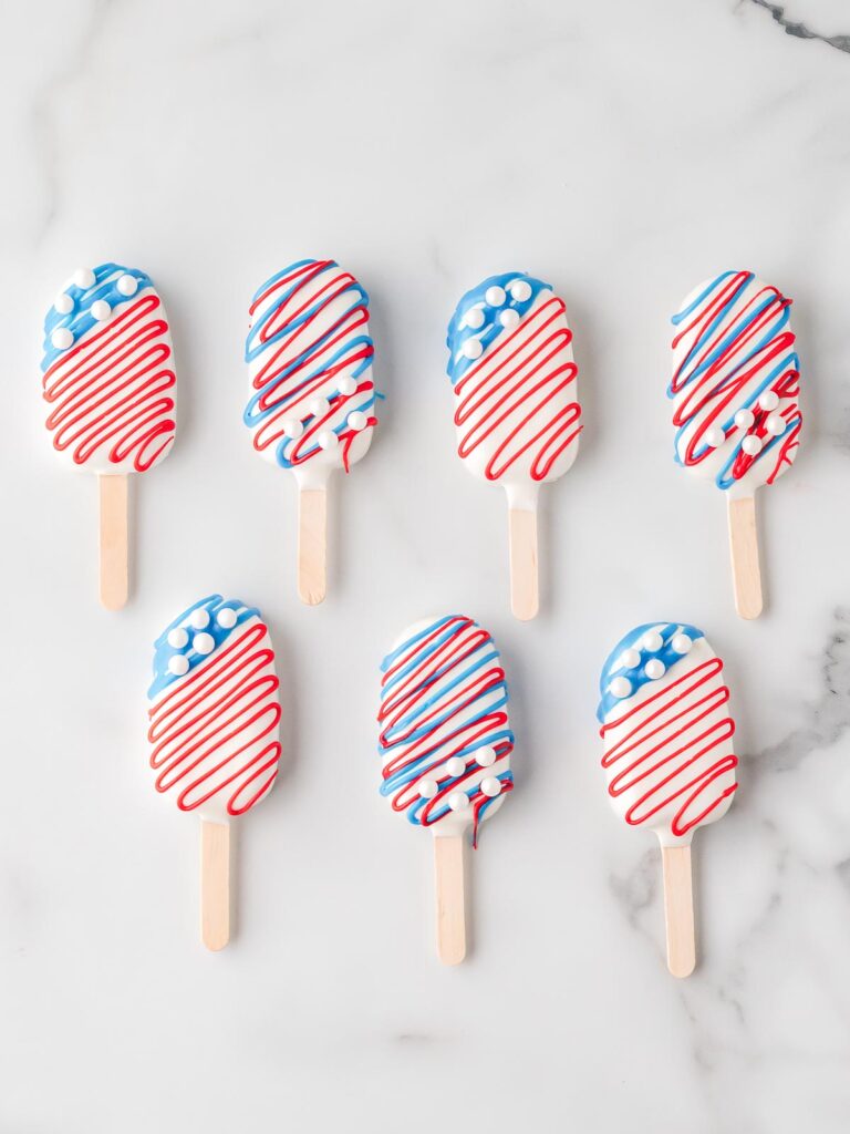Finished patriotic cakesicles decorated with red and blue drizzle and candy pearls, perfect for July 4th.