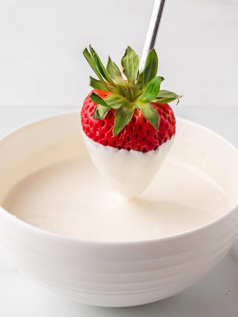 Fresh strawberry being dipped into melted white candy coating for red, white, and blue dessert.