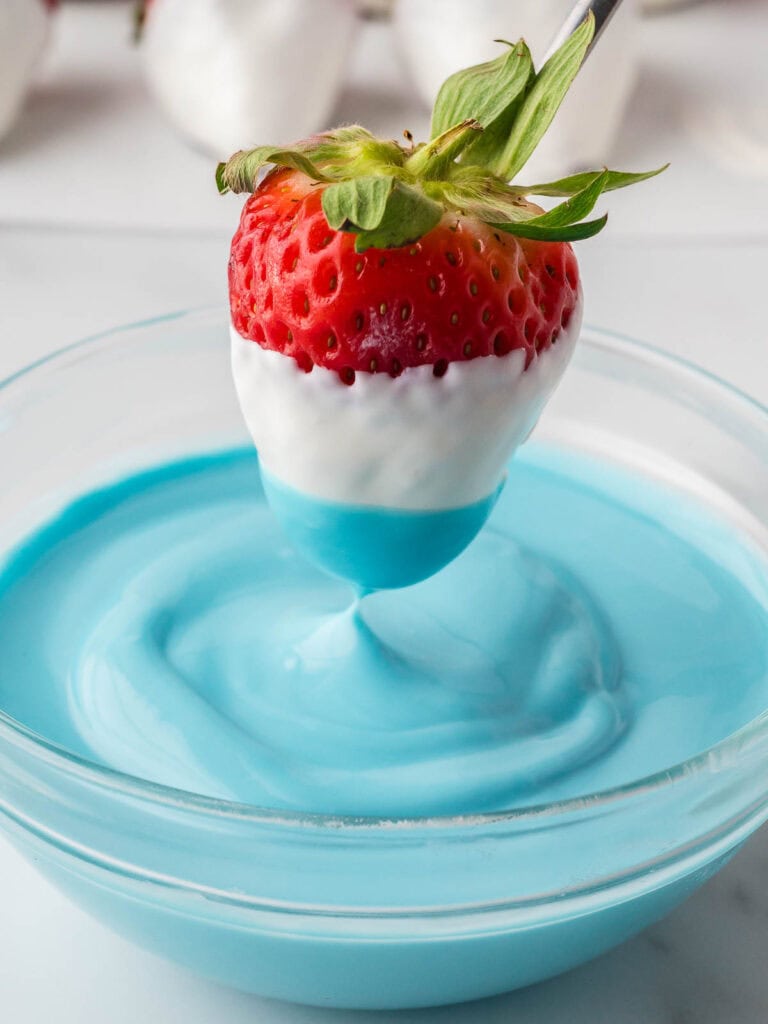 Strawberry already dipped in white candy, now being dipped into melted blue candy coating.