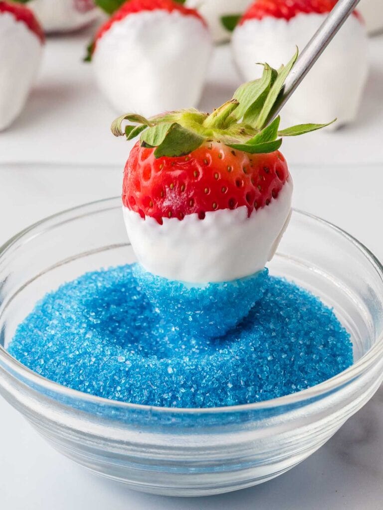 Strawberry dipped in white and blue candy melts being rolled in blue sanding sugar for a festive finish.