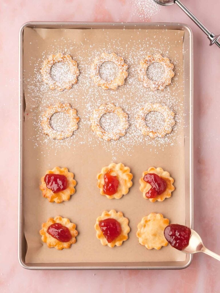 Bottom cookie halves with dollops of strawberry jam added, ready to be sandwiched.