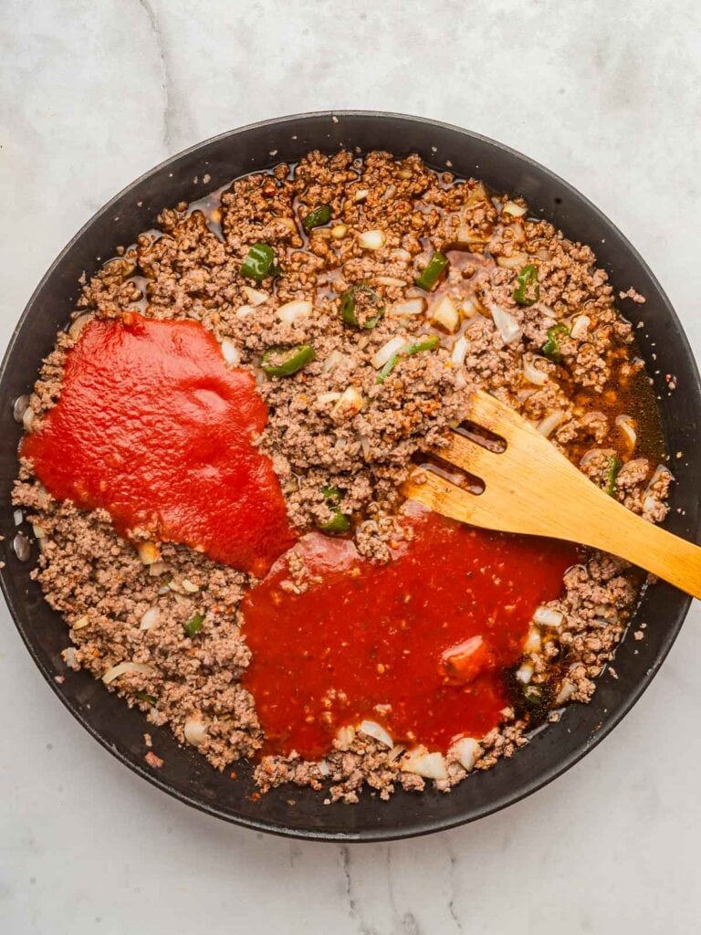 Enchilada sauce, tomato sauce, and broth added to the cooked beef and vegetables in the pan before mixing.