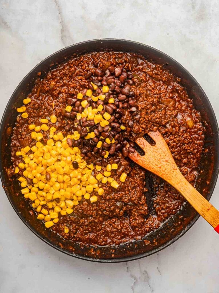 Corn and black beans added to the thickened taco mixture, sitting on top before being stirred in.