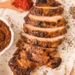 Sliced chipotle chicken on a white board with spices, garlic, and herbs scattered around.