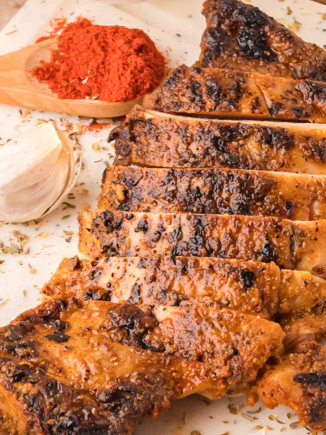 Close-up of grilled chipotle chicken slices with paprika, garlic, and dried oregano on the board.