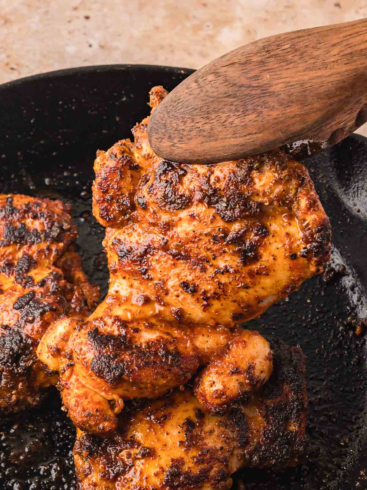 Juicy chipotle chicken thighs seared in a cast iron skillet with a wooden spoon lifting one out.