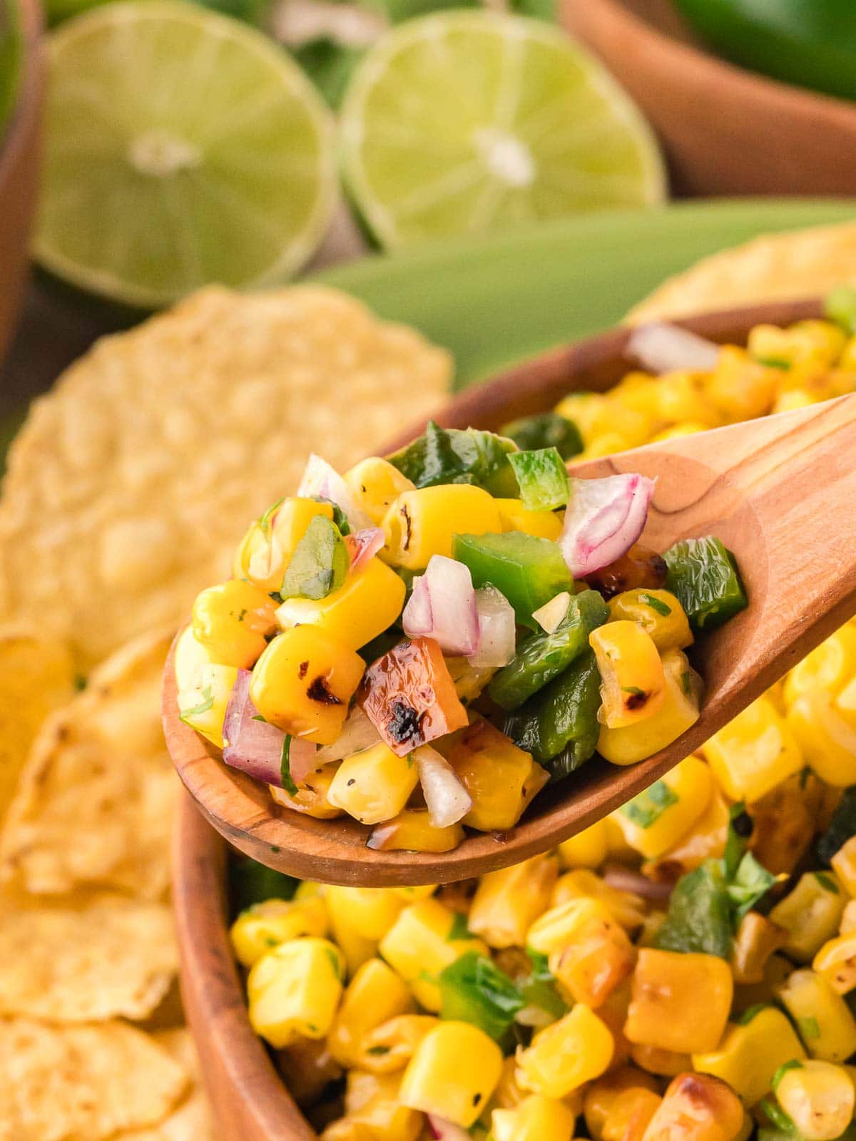 Close-up of a spoonful of roasted corn salsa with red onion, cilantro, and charred corn kernels, showing texture and color.