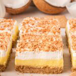 Close-up of a coconut cream bar showing graham cracker crust, thick coconut pudding, whipped topping, and golden toasted coconut.