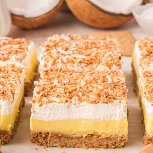 Close-up of a coconut cream bar showing graham cracker crust, thick coconut pudding, whipped topping, and golden toasted coconut.
