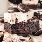 Bite taken out of a cookies and cream brownie bar with a creamy cheesecake topping and stacked mini Oreos on top.