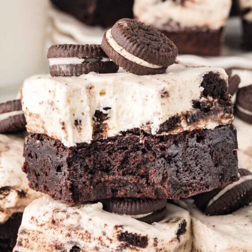 Bite taken out of a cookies and cream brownie bar with a creamy cheesecake topping and stacked mini Oreos on top.