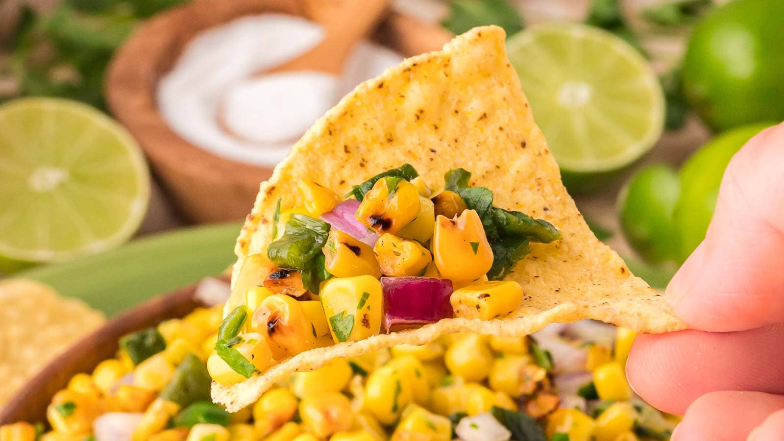 Close-up of a tortilla chip holding a spoonful of roasted corn salsa with red onion, cilantro, and charred corn kernels, showing texture and color.