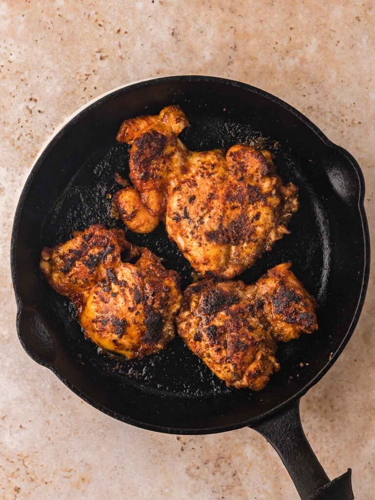 Three chipotle-seasoned chicken thighs cooking in a black cast iron skillet