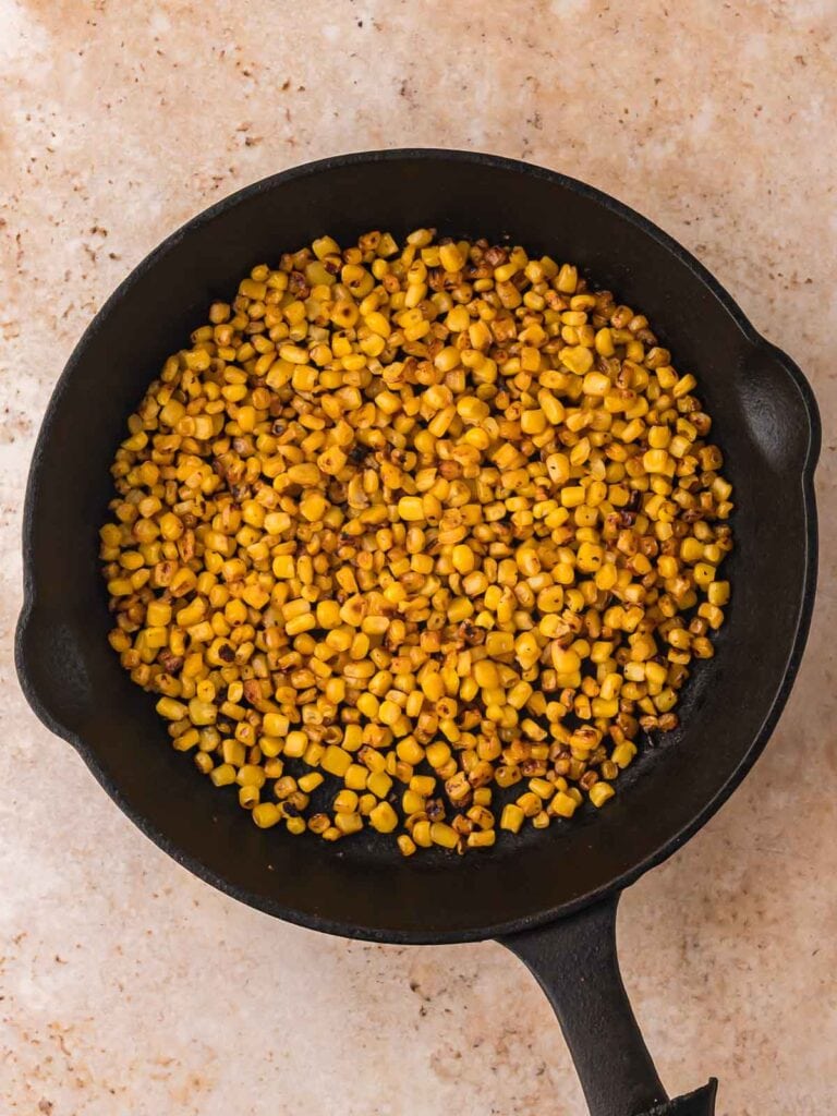 Canned corn charred in a cast iron skillet on the stovetop, showing the browning process for copycat Chipotle roasted corn salsa.