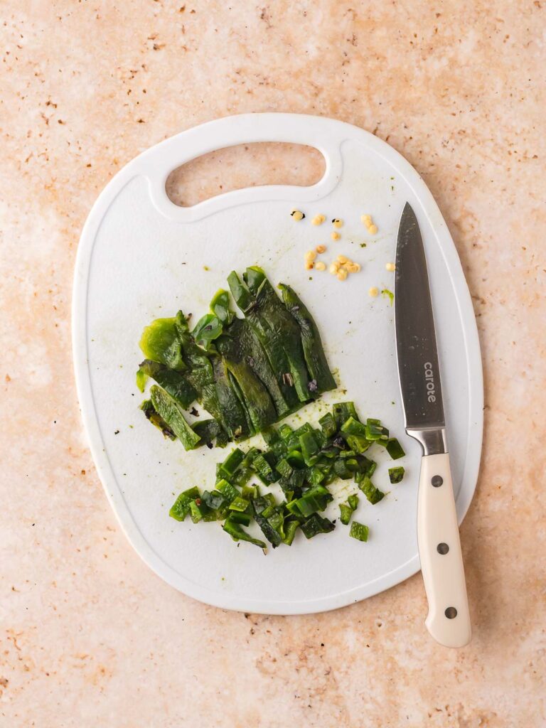 Chopped roasted poblano pepper on a white cutting board with knife beside it, prepared for mixing into the salsa.