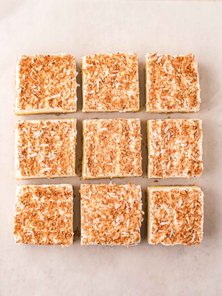 Nine coconut cream bars sliced and arranged on parchment, showing clean layers and toasted topping.