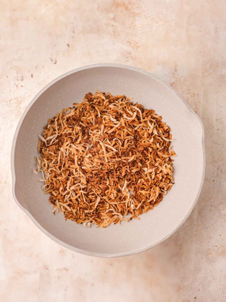Golden brown shredded coconut toasting in a nonstick pan on a light countertop.