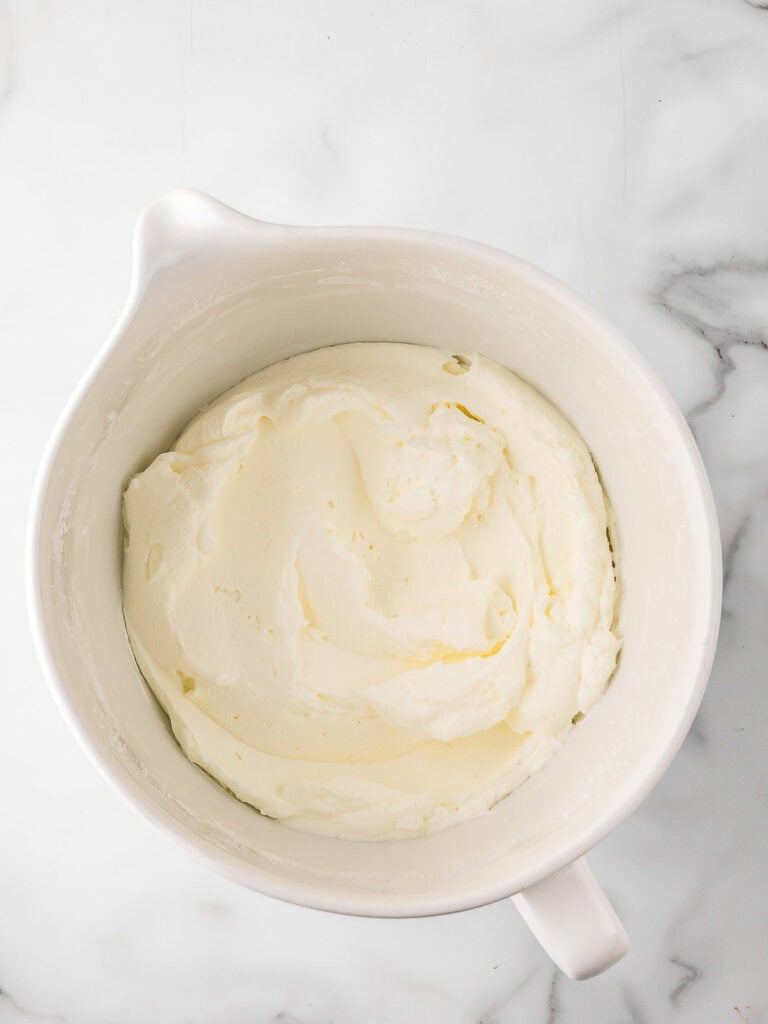 Whipped cream in a white mixing bowl, ready to fold into the cream cheese base.