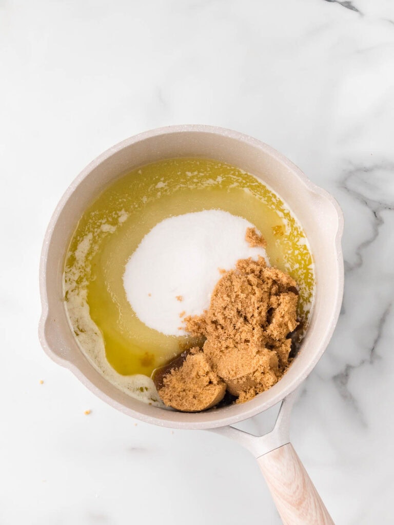 Melted butter with granulated and brown sugar in a saucepan on a marble counter.