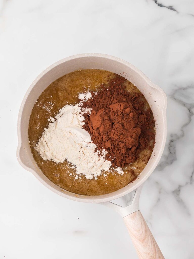 Cocoa powder and flour added to the wet brownie mixture before stirring.