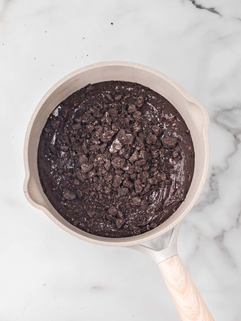 Roughly chopped Oreo cookies sitting on top of the mixed brownie batter in the pot.