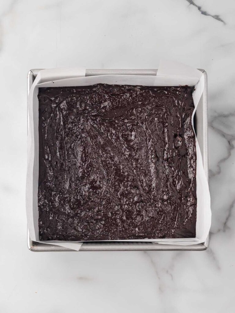 Brownie batter spread evenly into a parchment-lined square baking pan.