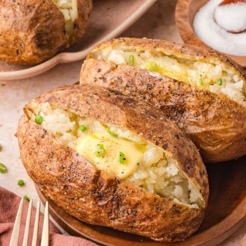 Two seasoned baked potatoes on a brown plate, served with a small bowl of salt in the background.
