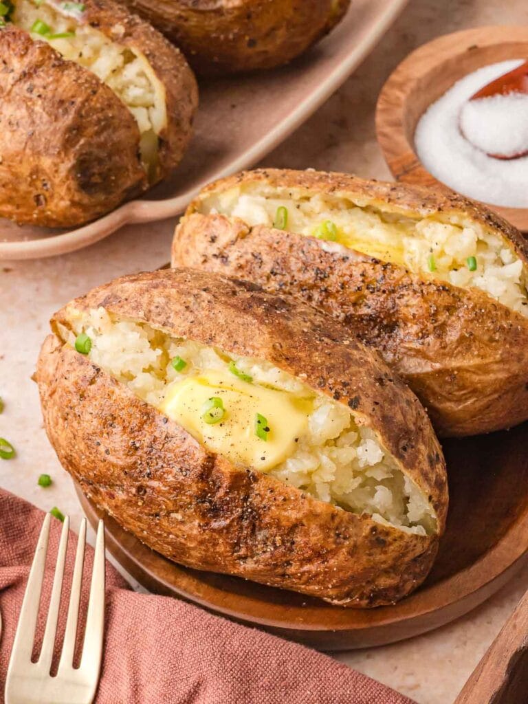Two seasoned baked potatoes on a brown plate, served with a small bowl of salt in the background.
