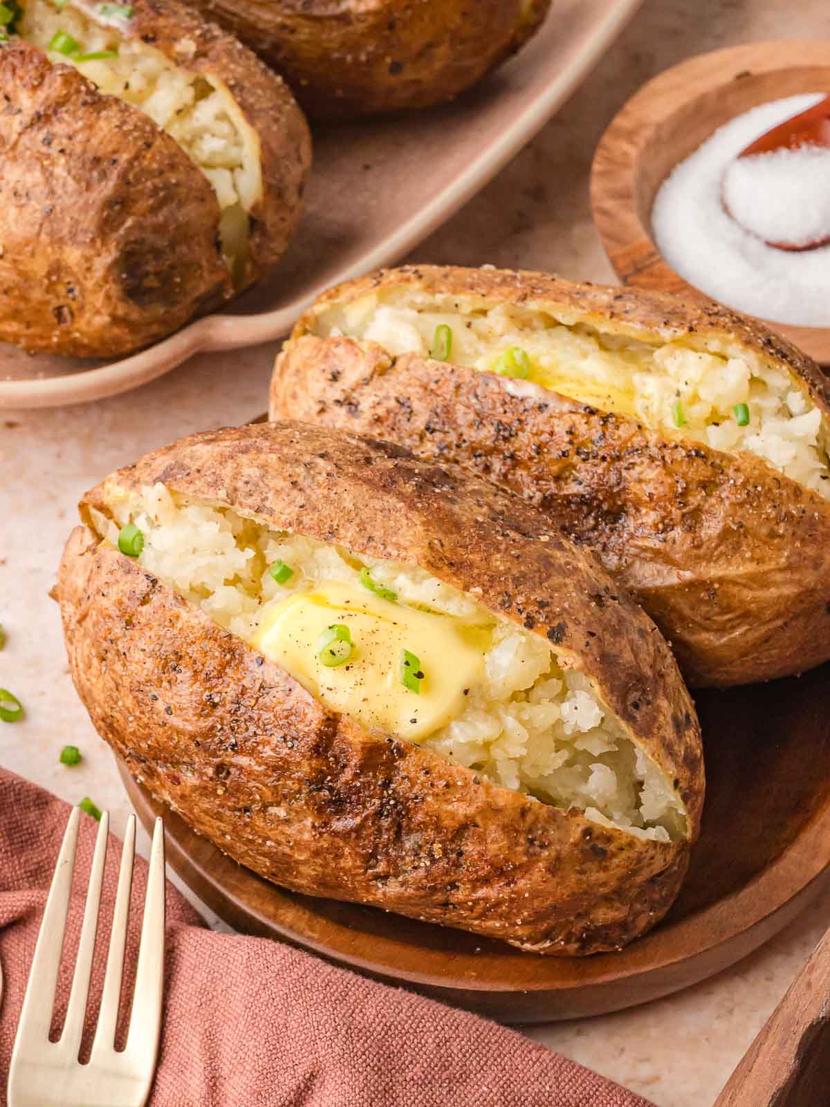 Two seasoned baked potatoes on a brown plate, served with a small bowl of salt in the background.